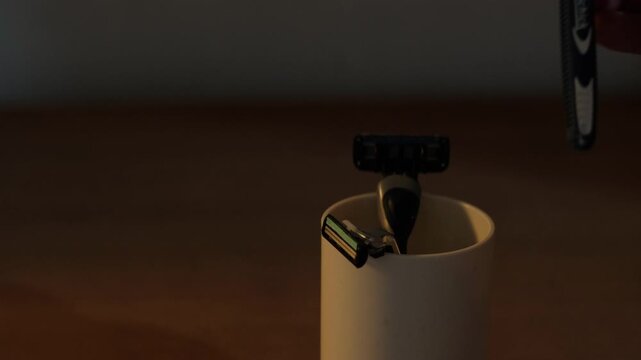 Hand placing manual razor in a cup with other safety razors indoors - static medium shot