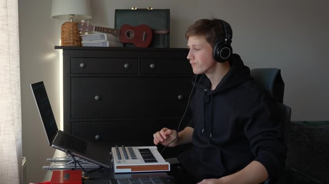 Music producer in their home studio puts on studio headphones, preparing to start a session using a laptop DAW, MIDI controller, and Focusrite audio interfacesic, static shot