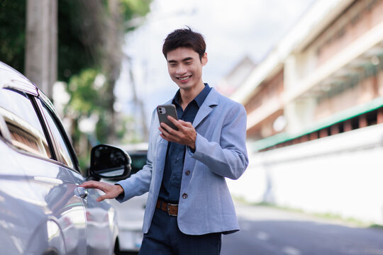 Young asian man using phone app getting into car
