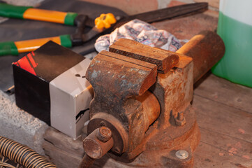 Close-up of an old rusty vise with tools and other objects on a wooden surface