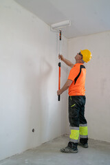 A construction worker paints a ceiling with a wide, specialized paint roller. Apartment renovation.