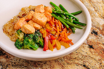 Healthy salmon and vegetable bowl with noodles on a stone countertop