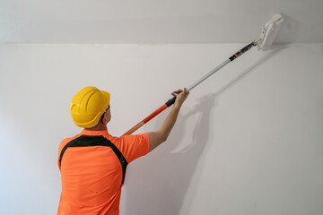 A construction worker paints a wall with a wide, specialized paint roller. Apartment renovation.