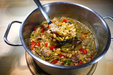 Rustic hearty stew in a cooking pot made from beans, pork and bell peppers, homemade meal for autumn and winter, selected focus