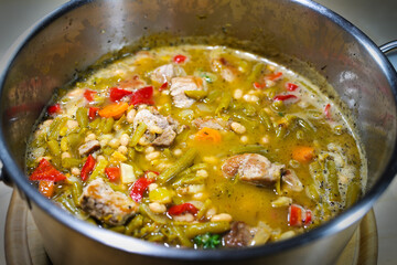 Bean stew with pork meat and bell pepper in a stainless steel pot, rustic homemade meal or pre-cooking for food-storage, selected focus