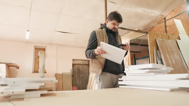 Skilled man in a workshop examines wooden panels while holding a measuring tool, showcasing craftsmanship and attention to detail, camera pans across the workspace