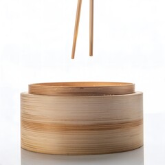 Chopsticks poised above a bamboo steamer basket, ready to pick up food in a clean, minimalist composition against a bright background.