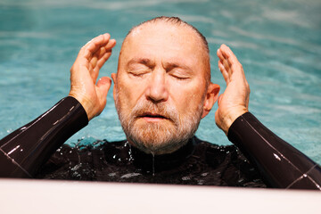 Senior diver in wetsuit preparing to dive in swimming pool