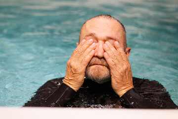 Senior diver in wetsuit touching eyes in swimming pool 