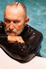 Portrait of senior diver in wetsuit looking at camera near poolside 