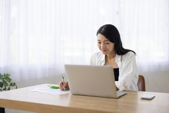 Woman Taking Notes on Paper While Working on Laptop