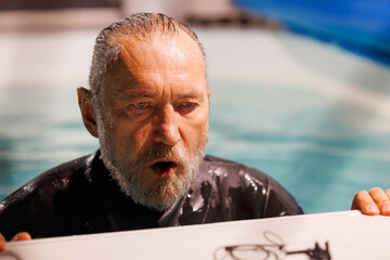 Portrait of senior diver breathing near nose clip on poolside 