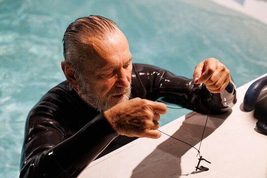 Senior diver in wetsuit holding nose clip at poolside 