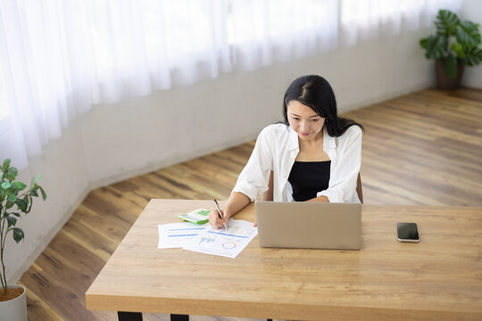 Woman Taking Notes on Paper While Working on Laptop