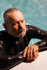 Grey haired free diver in wetsuit using nose clip at poolside 