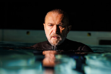 Portrait of senior free diver in wetsuit looking at camera in swimming pool 
