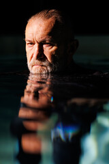 Portrait of senior free diver looking at camera over water surface in swimming pool 