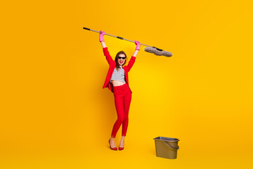 Charming young woman in a red suit holding a mop celebrating on a vibrant yellow background