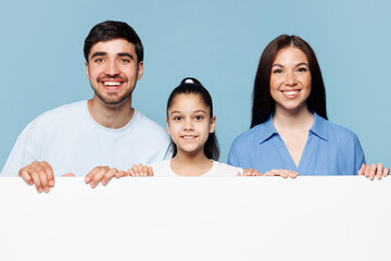 Young fun parents mom dad with child kid daughter girl wearing casual clothes hold blank sign board poster for promotional content place for text isolated on plain blue background. Family day concept.