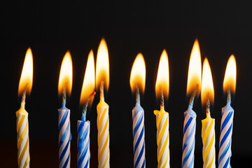 Yellow and blue birthday candles burning with soft warm flames on black background with copy space. Festive candles composition symbolizing celebration, joy, and bright holiday mood.