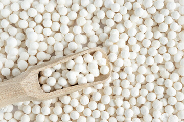 White dry tapioca pearls in wooden scoop on tapioca background. Top view of raw tapioca starch balls used for bubble tea or desserts. Tapioca pearls as healthy gluten free ingredient.