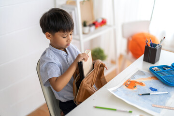 Asian boy getting ready for back to school preparation organizing books and stationery into school backpack at home, learning readiness, education, educational for parenting, kids ready to learning