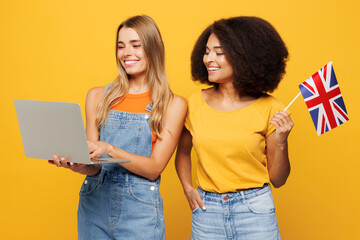 Two young friends buddies IT women wear denim casual clothes together hold American flag use work on laptop pc computer isolated on plain yellow orange background studio portrait. Lifestyle concept.