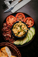Gourmet avocado toast with fried egg, tomato slices and mixed greens. Rustic food styling on a dark background, ideal for restaurant menus, healthy eating concepts and editorial content.