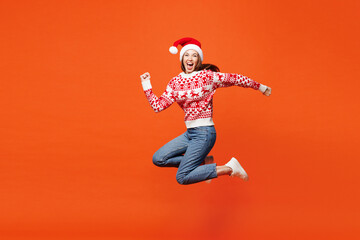 Obraz na płótnie Canvas Full body side profile view merry young woman wear red Christmas sweater Santa hat posing jump high run fast hurry up isolated on plain orange background Happy New Year celebration holiday concept.