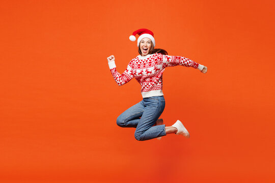 Fototapeta Full body side profile view merry young woman wear red Christmas sweater Santa hat posing jump high run fast hurry up isolated on plain orange background Happy New Year celebration holiday concept.