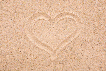 Drawn heart shape on dry light brown sea sand background. Closeup. Love concept. Closeup. Top down view.