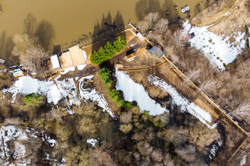 Drone view of swollen river breaching beach area during springtime thaw, brown water covering lowlands with remnants of snow on banks