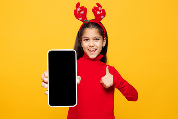 Merry little girl wear red clothes fun decorative deer horns on head posing hold use blank screen...