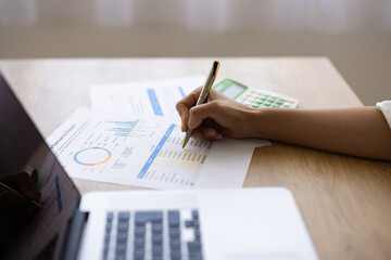 Close-up of Hand Writing on Business Report with Laptop and Calculator