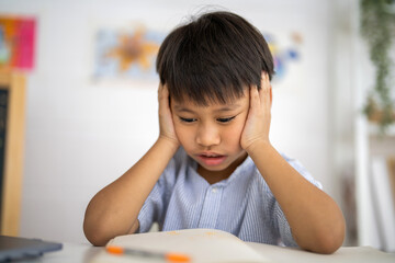 Asian boy stressed homework studying with hands on head, tired expression shows school pressure from parents, education overload with books, online learning, academic pressure and homework frustration