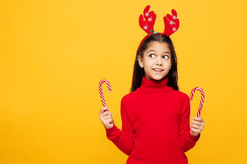 Merry little girl wears red clothes fun decorative deer horns on head posing hold in hand candy...