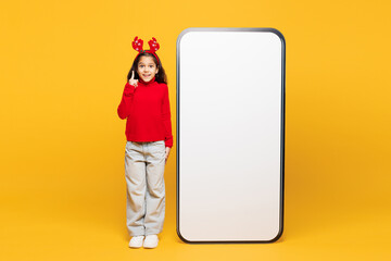 Full body merry little girl wear red clothes decorative deer horns on head big huge blank screen...