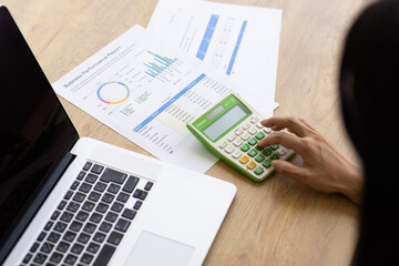 Close-up of Hand Using Calculator with Business Report and Laptop
