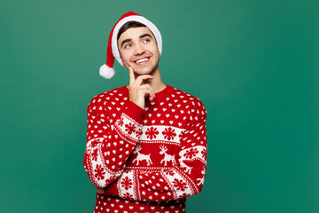 Merry young man wears red warm cozy Christmas sweater Santa Claus hat posing put hand prop up on...