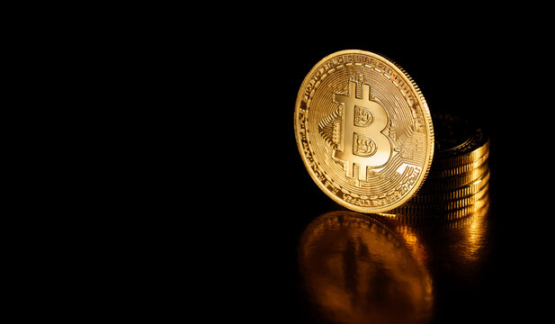 Bitcoin coin isolated on black background. Stack of gold coins with Bitcoin coin in front of it. Golden Bitcoin, crypto currency. Cryptocurrency and electronic decentralized money concept.