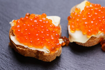 Sandwiches with red caviar on black slate stone plate. A delicious appetizer of trout caviar on a slice of bread with cream cheese. Salted salmon fish roe for fish delicacy concept.