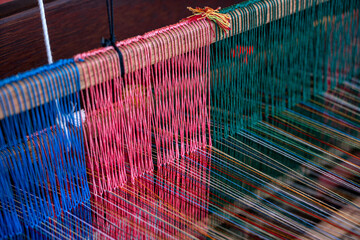 Doha, Qatar - December 01, 2025: Traditional hand-weaving in progress, showing a close-up view of colorful threads arranged on a wooden loom. A craftsman&rsquo;s hands guide the weaving process.