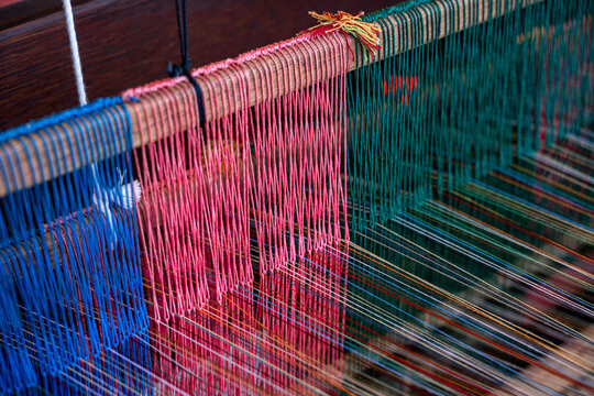 Doha, Qatar - December 01, 2025: Traditional hand-weaving in progress, showing a close-up view of colorful threads arranged on a wooden loom. A craftsman’s hands guide the weaving process.