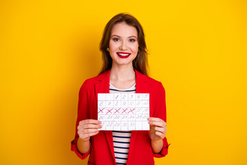 Confident young woman holding a marked calendar, stylish outfit and vibrant yellow background