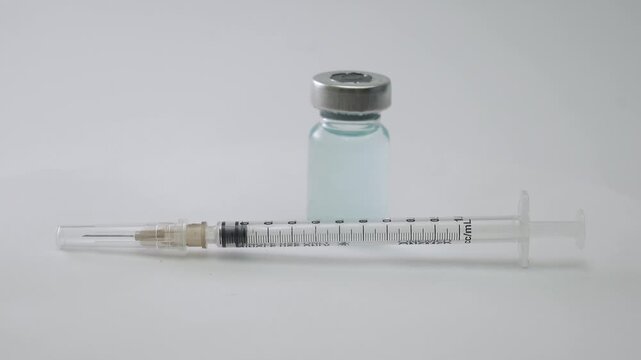 Medical syringe and liquid medicine vial placed on a rotating table against a clean white background. Medical Syringe and Vaccine Vial