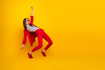 Modern young woman in a vibrant red suit striking an expressive pose against a yellow background, showcasing trendy fashion style