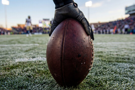 Player grips football on frosty field at sunset before kickoff, focus on leather texture and game preparation in outdoor stadium with competitive sports atmosphere