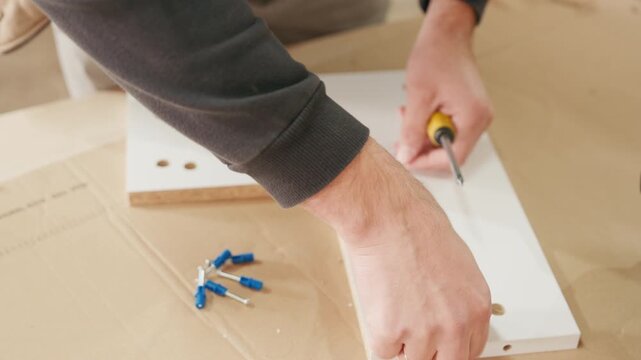 Hands assembling furniture piece with screws and connectors on a work surface, showcasing detailed craftsmanship, camera zooms in on the assembly process