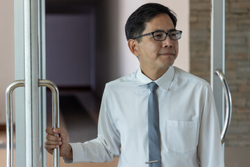 Back or rear view of South East Asian office worker, business man walking in to the office, opening the door