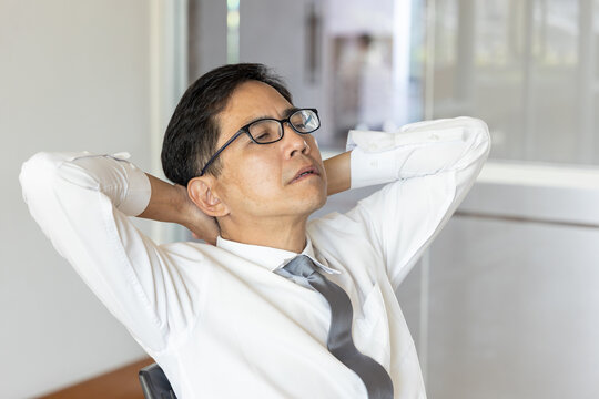 Overworked, tired, stressed South East Asian businessman or office worker resting in the meeting room